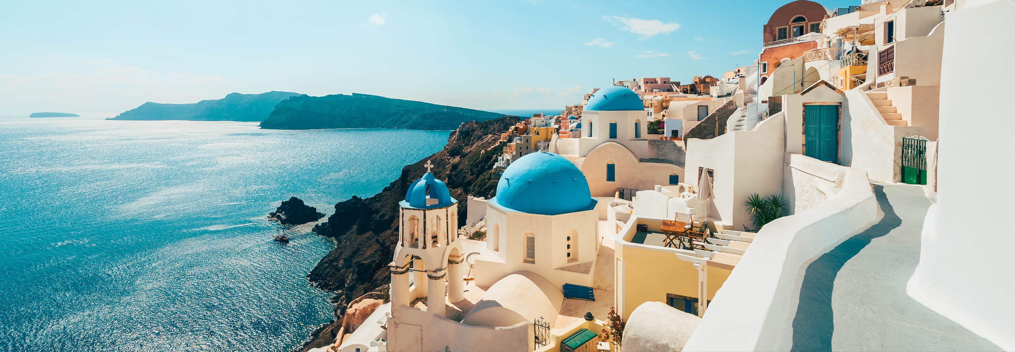 Blue domes of Oia, Greece, rise above white buildings, showcasing the village's stunning architecture against a clear sky