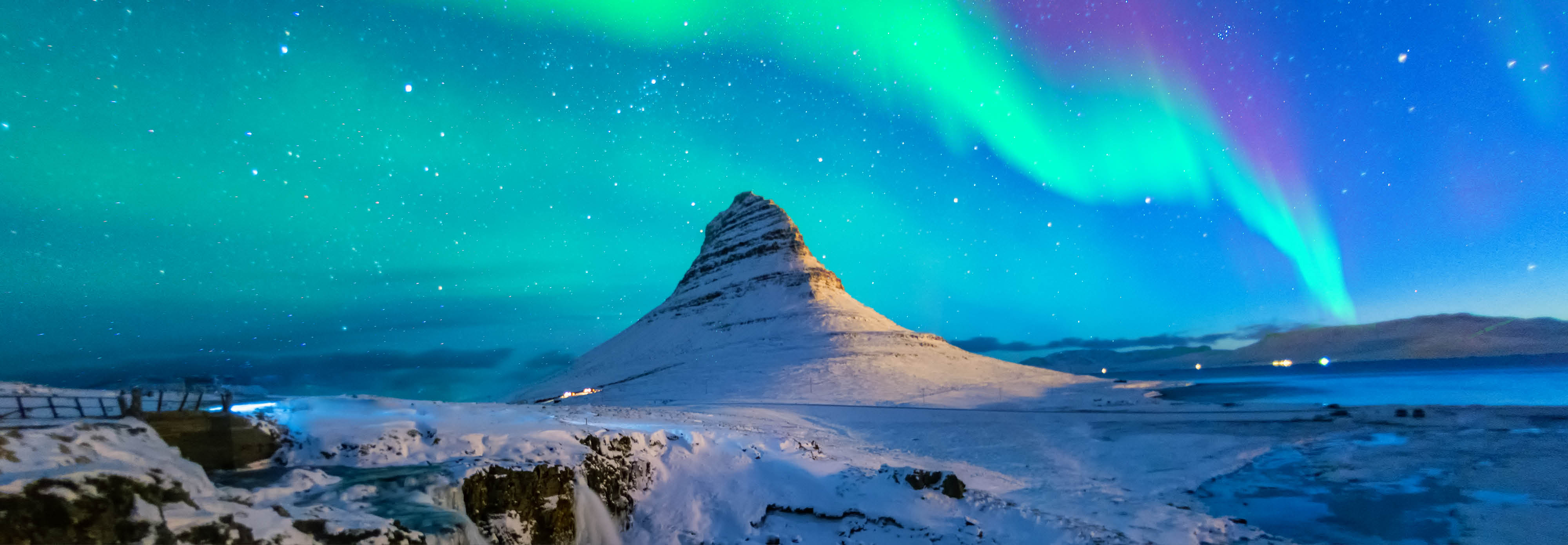 The aurora borealis illuminates the night sky above a majestic mountain landscape in Iceland