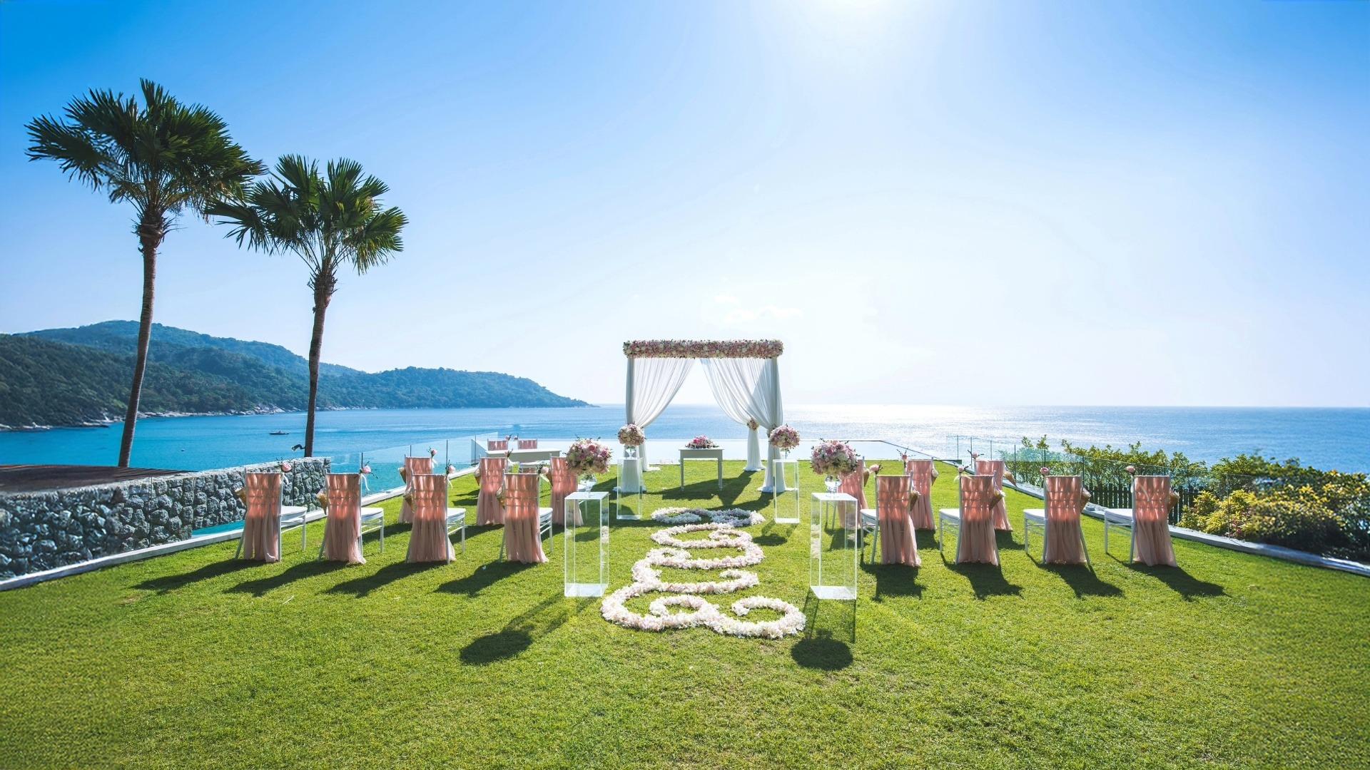 Outdoor wedding altar with pink chairs on lawn facing ocean view
