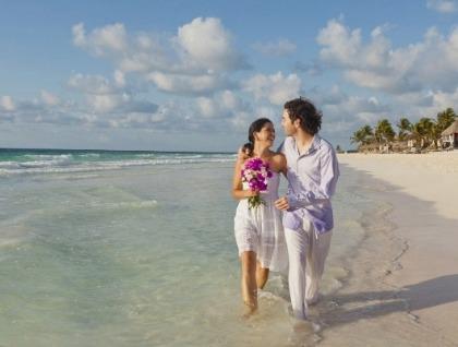 Smiling couple walks along sandy beach, woman holding purple flowers