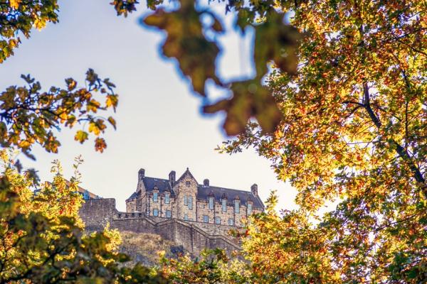 Stone castle on a hill framed by trees with autumn leaves.