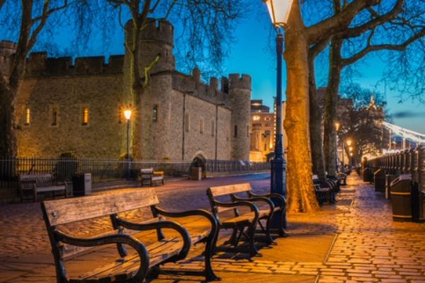 Stone castle with benches and lamplights along a cobblestone path at dusk.