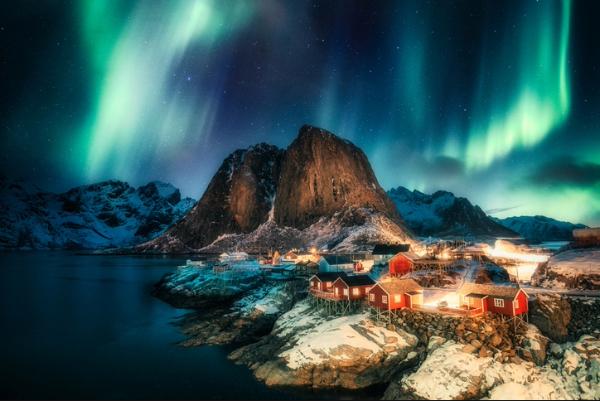 Colorful northern lights glowing above snowy mountain village at night