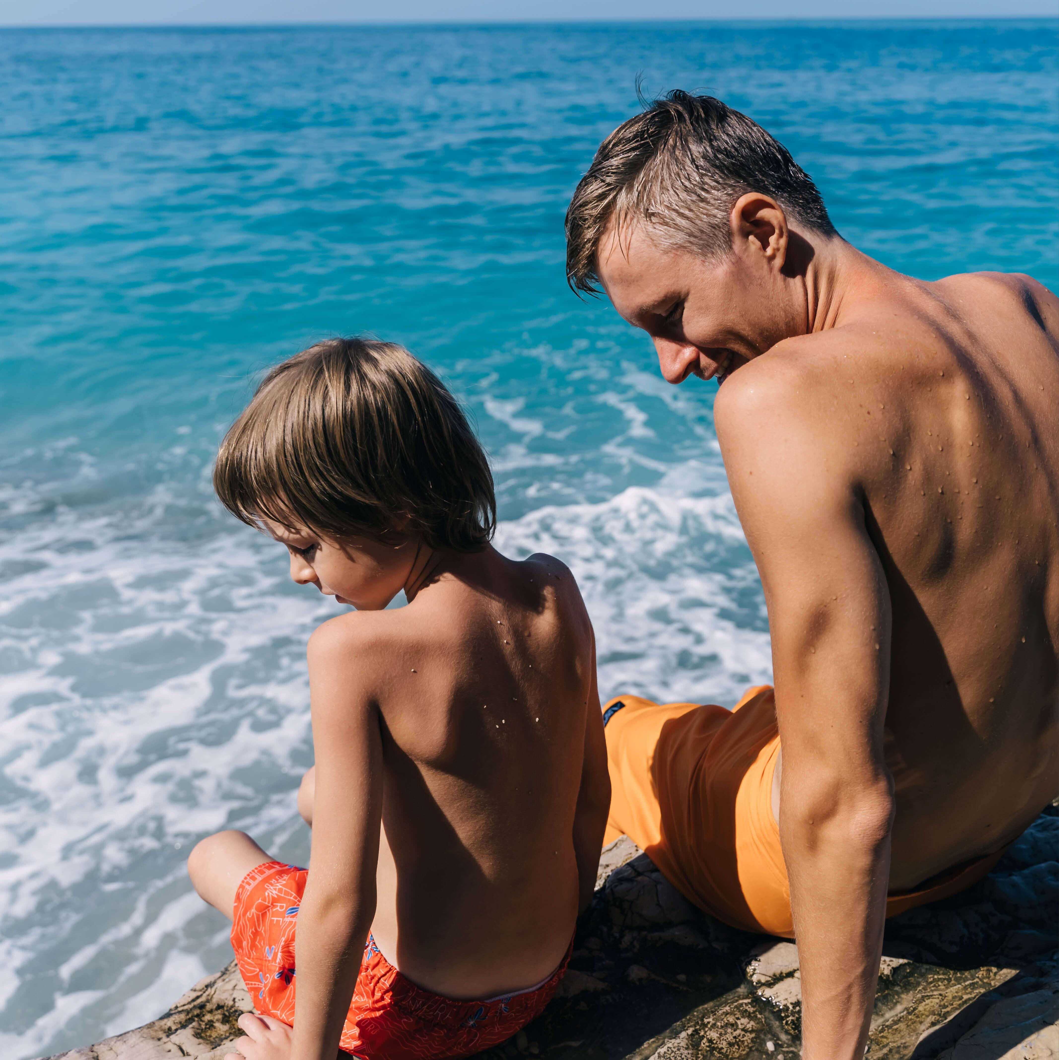 A father and son sit along the ocean on vacation in Anguilla