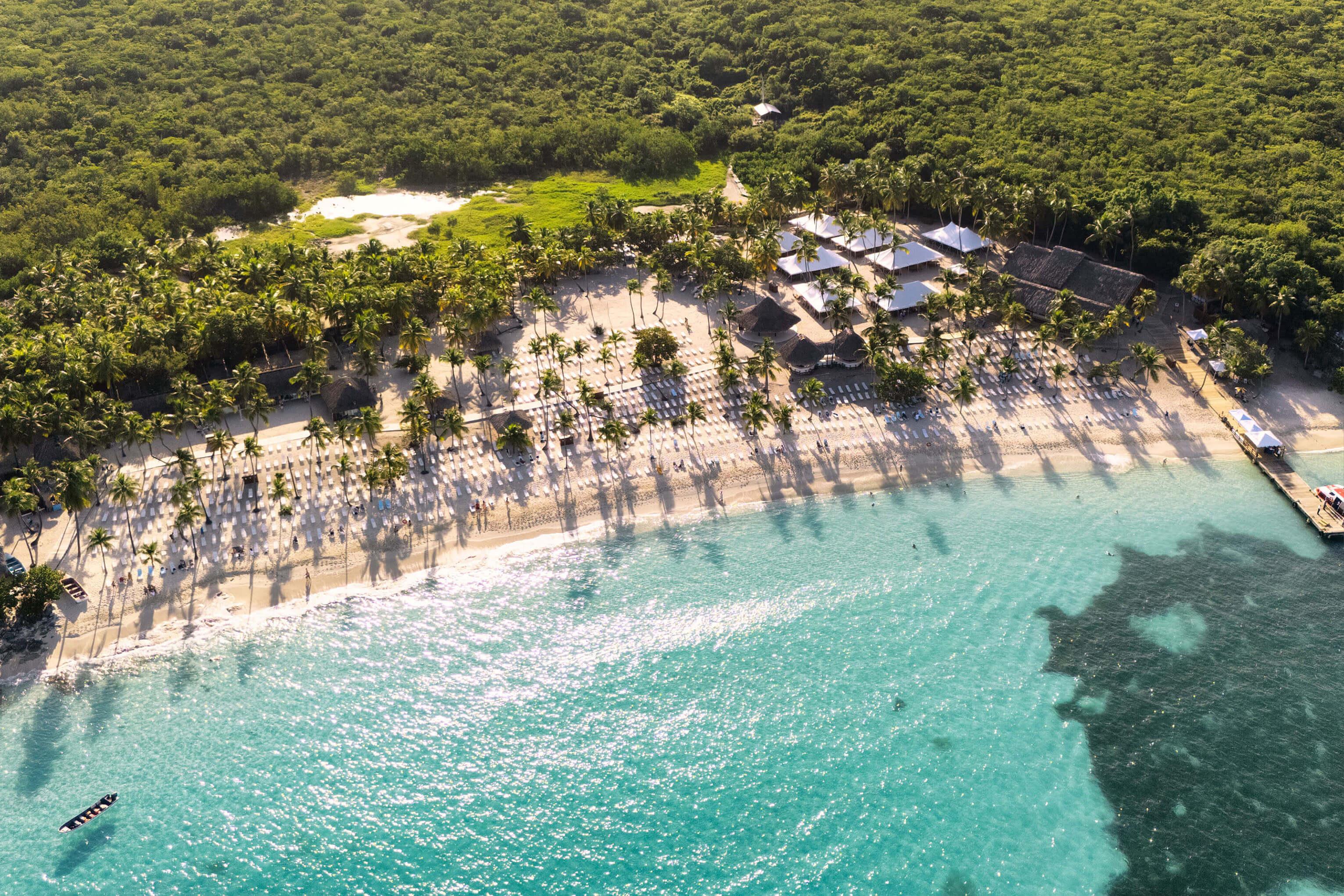 Overhead perspective of a beach and resort in the Dominican Republic, showcasing sandy shores, clear blue water, and tropical landscaping