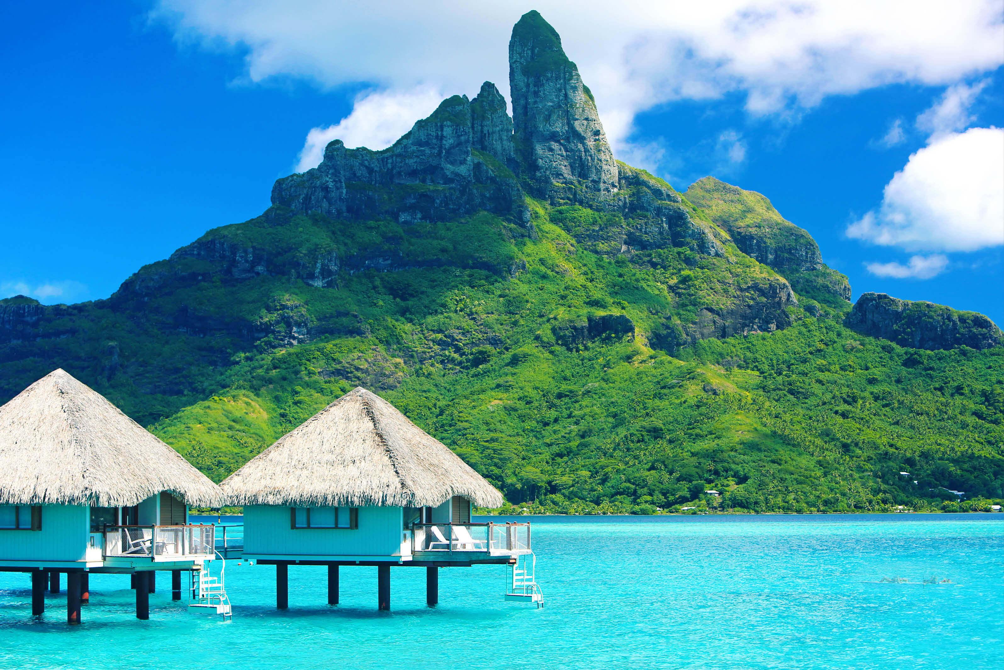 Overwater bungalows in Tahiti on bright azure water with view of unique mountain in distance