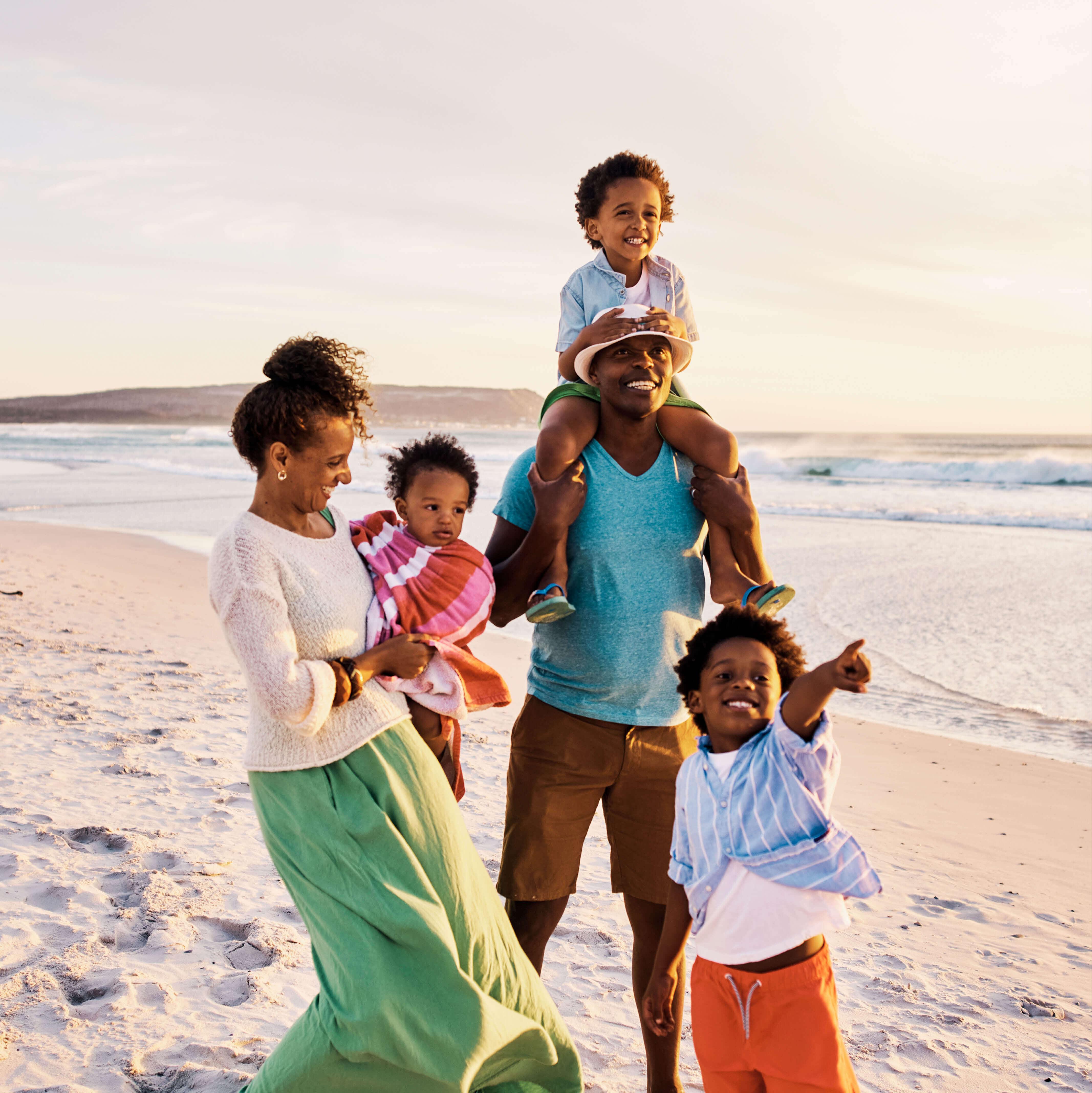 A family of 5 walks laughs while walking along the beach at sunset
