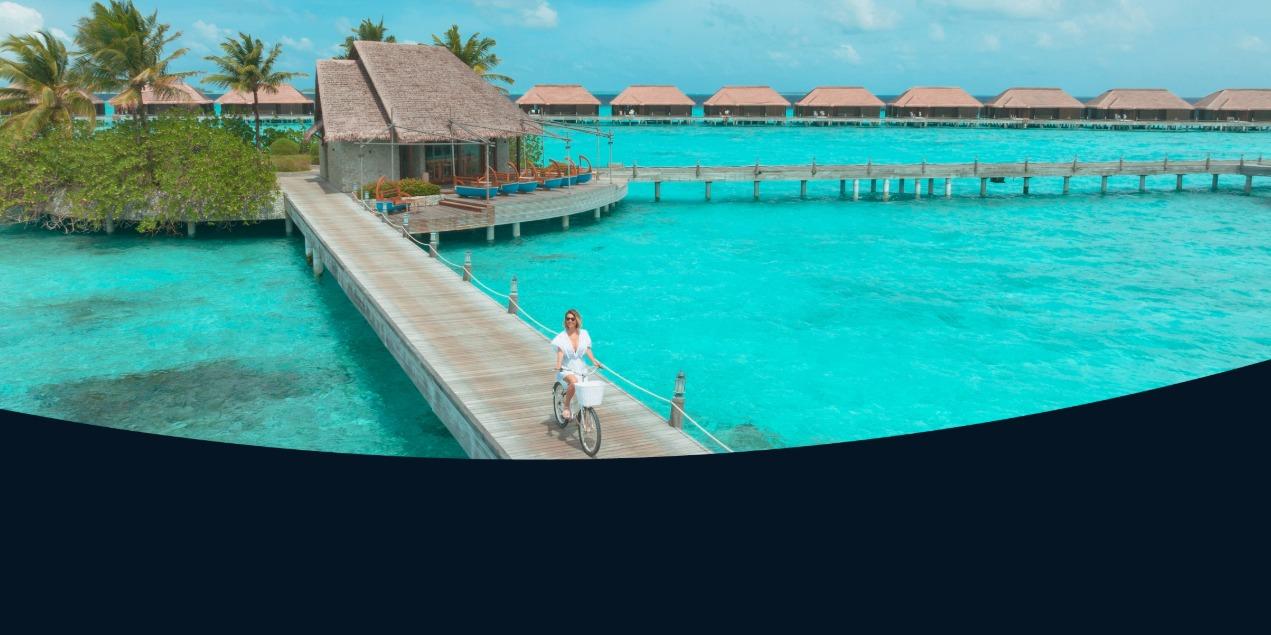 Woman riding a bicycle along an overwater boardwalk at a tropical resort