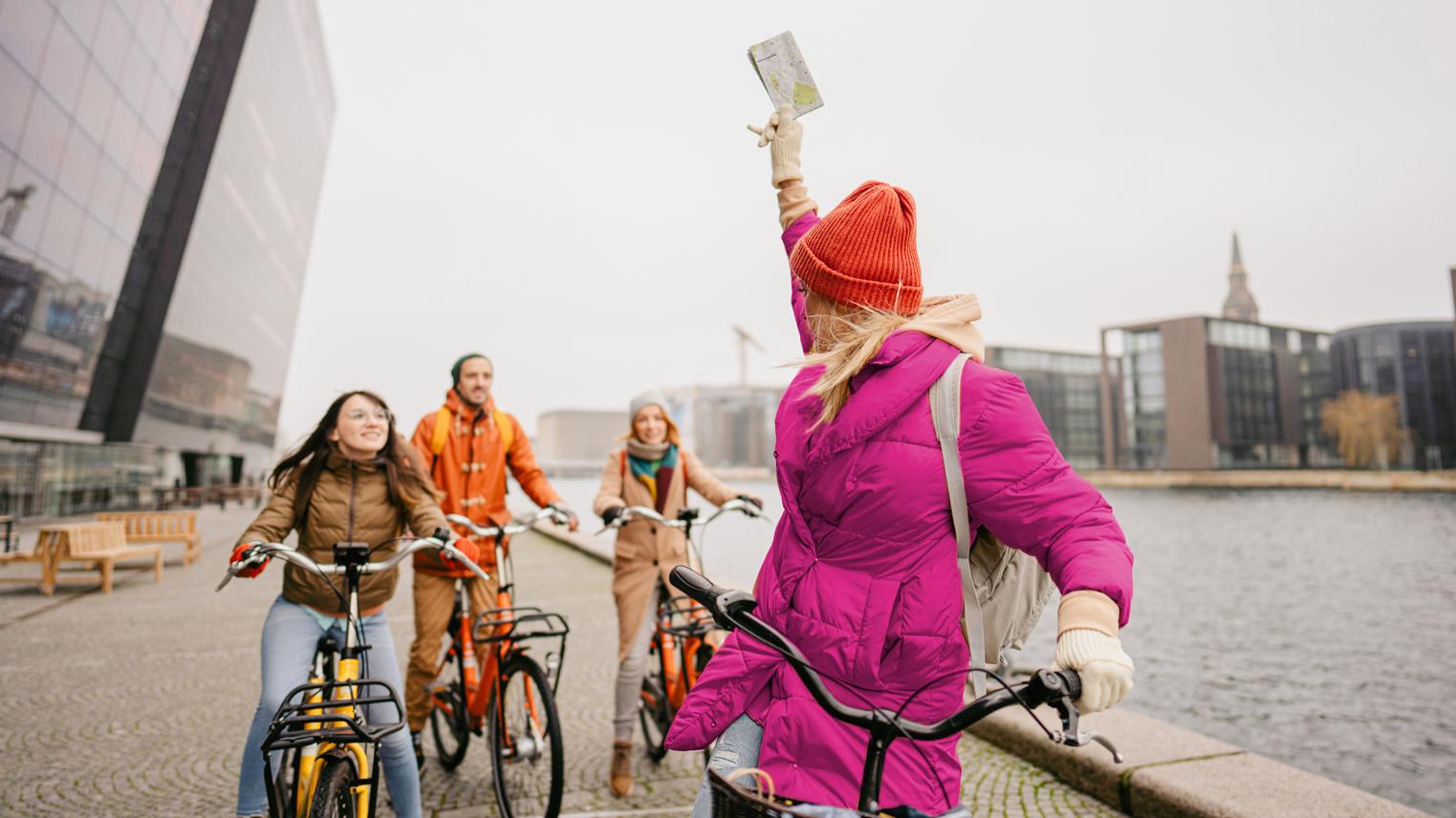 Three women and a man ride bikes along a river
