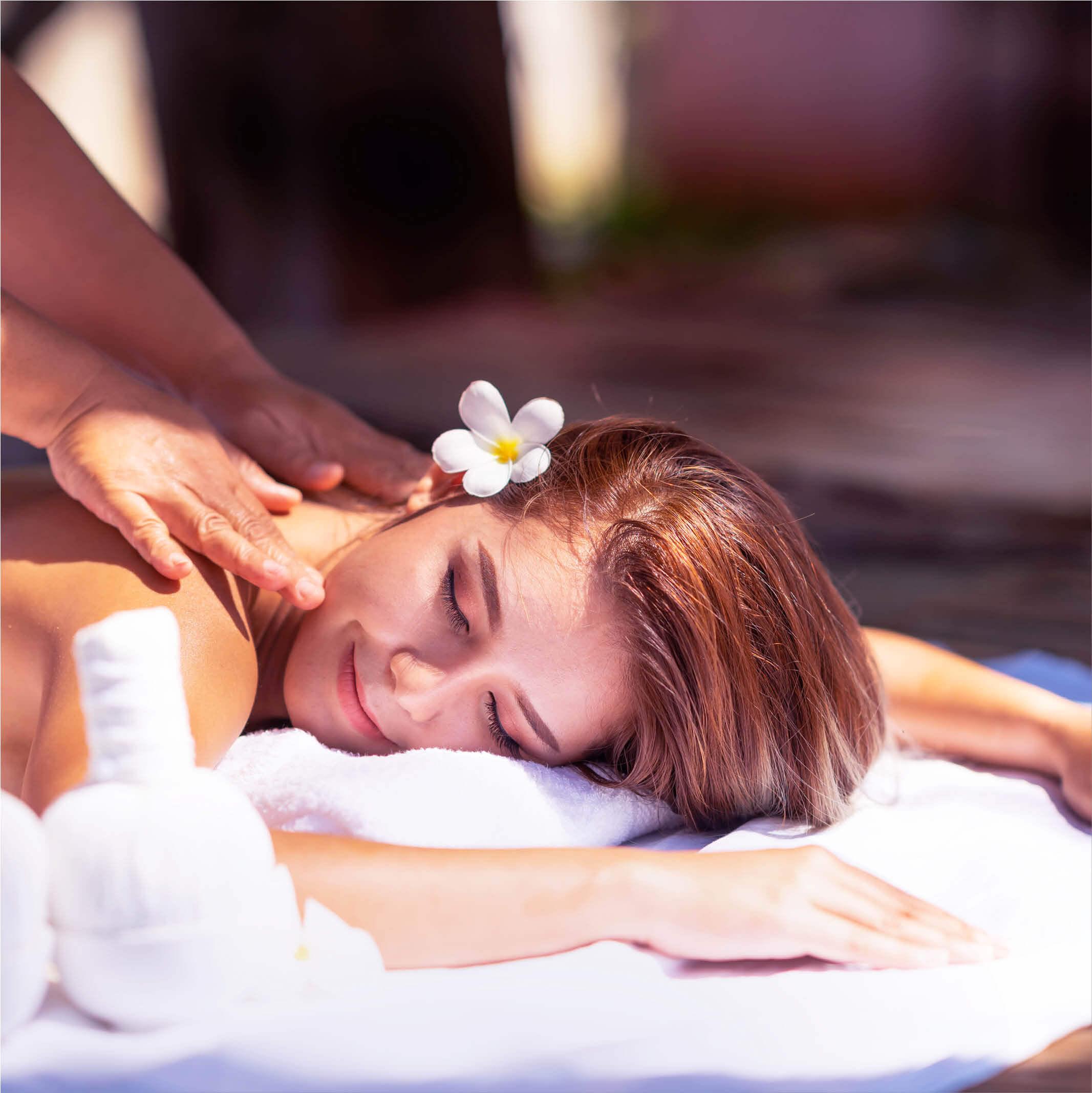 A woman with a flower in her hair relaxes during a massage at a spa