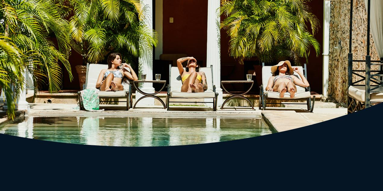 Three women lounge by a pool in a tropical setting