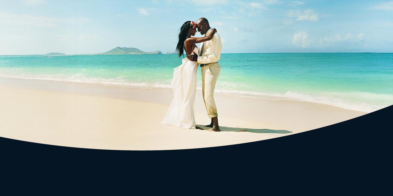 A newlywed couple in a wedding dress and suit embraces on a scenic beach