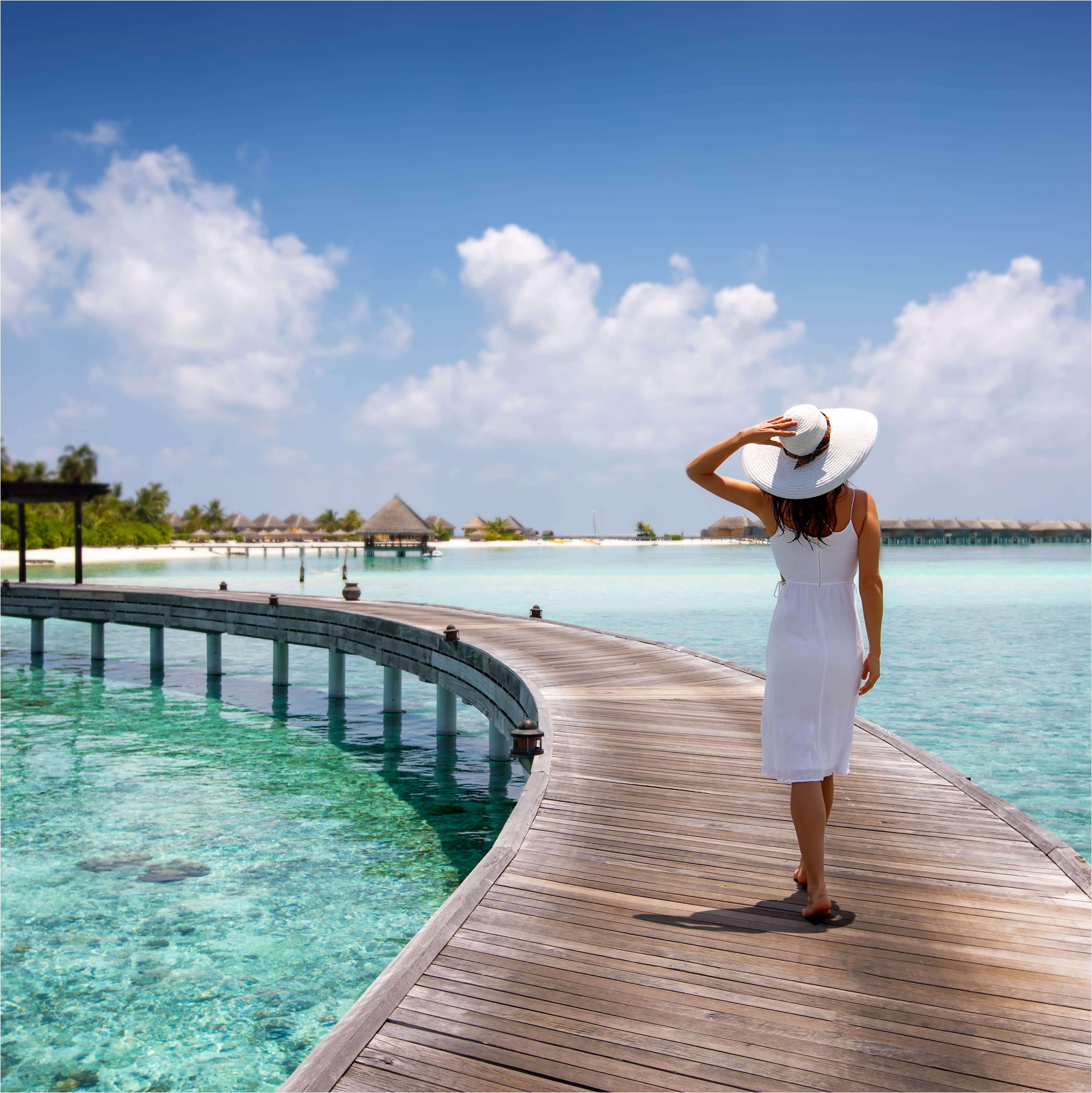 A woman in a white dress and hat walks along an over-the-water walkway