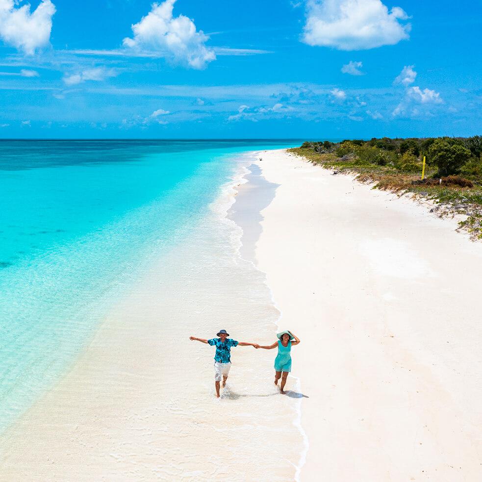 A pair of travelers run along a pristine Caribbean shoreline