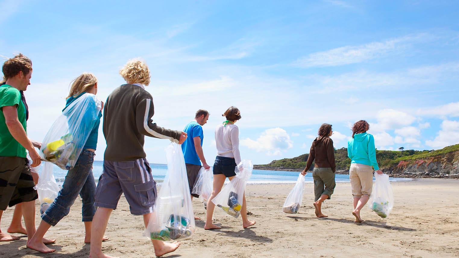 A volunteer group walk along the beach with trash bags