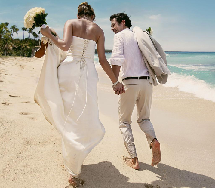 A bride and groom walk along a beach